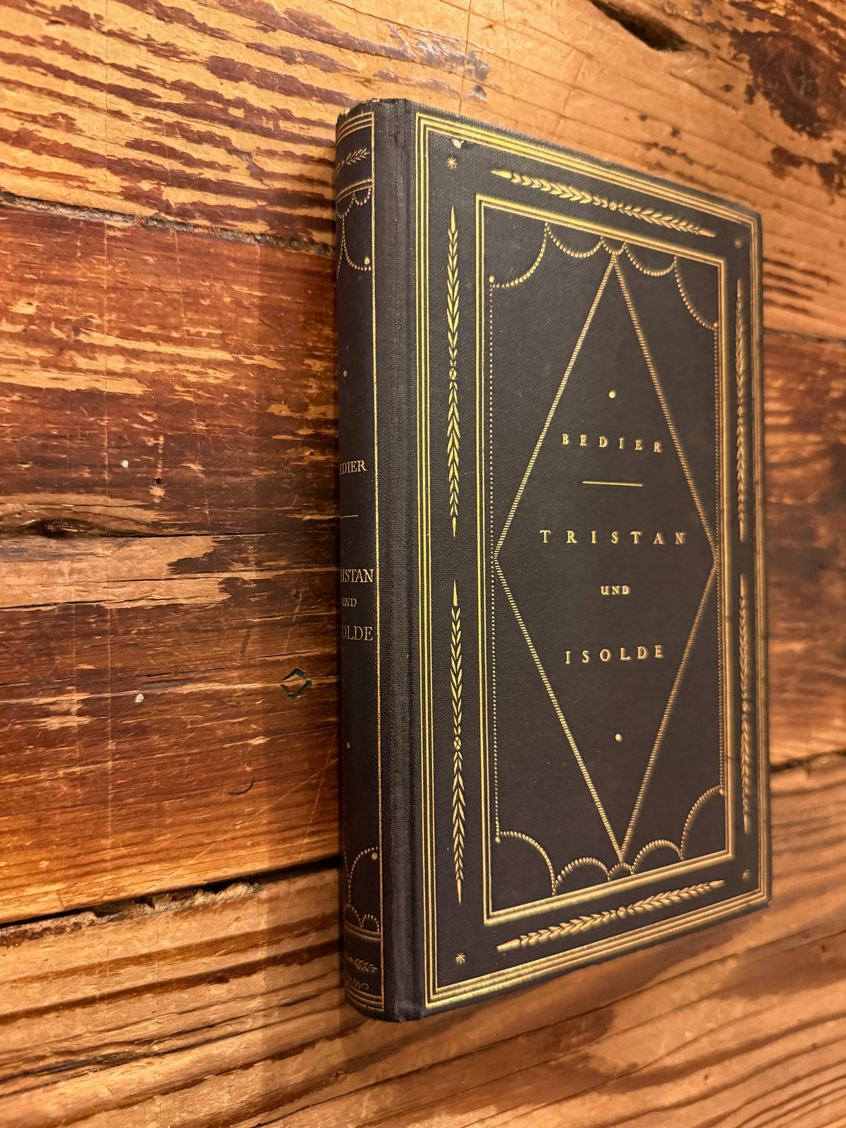 Front cover and spine of book in German titled 'Tristan und Isolde' by Joseph Bédier, published in 1923, exposed on a wooden surfacer 