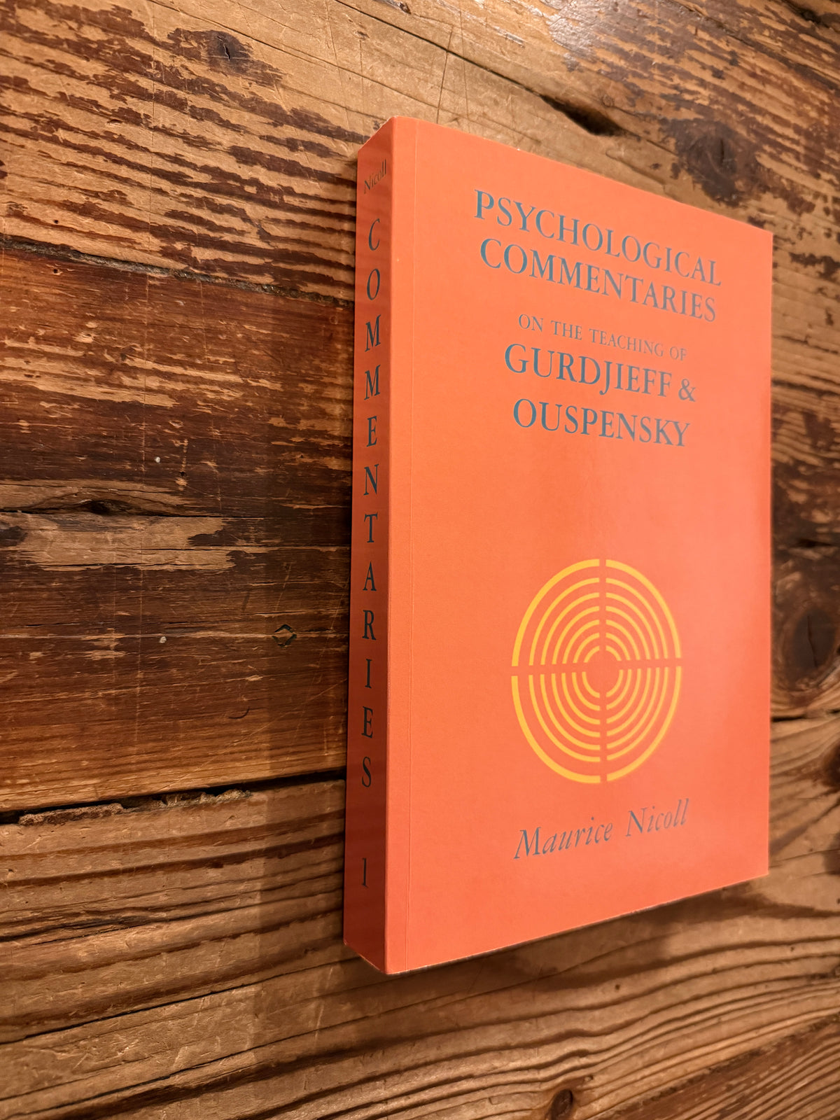 Front cover and spine of a book titled 'Psychological commentaries on the teaching of Gurdjieff & Ouspensky, vol I' by Maurice Nicoll lying on wooden surface