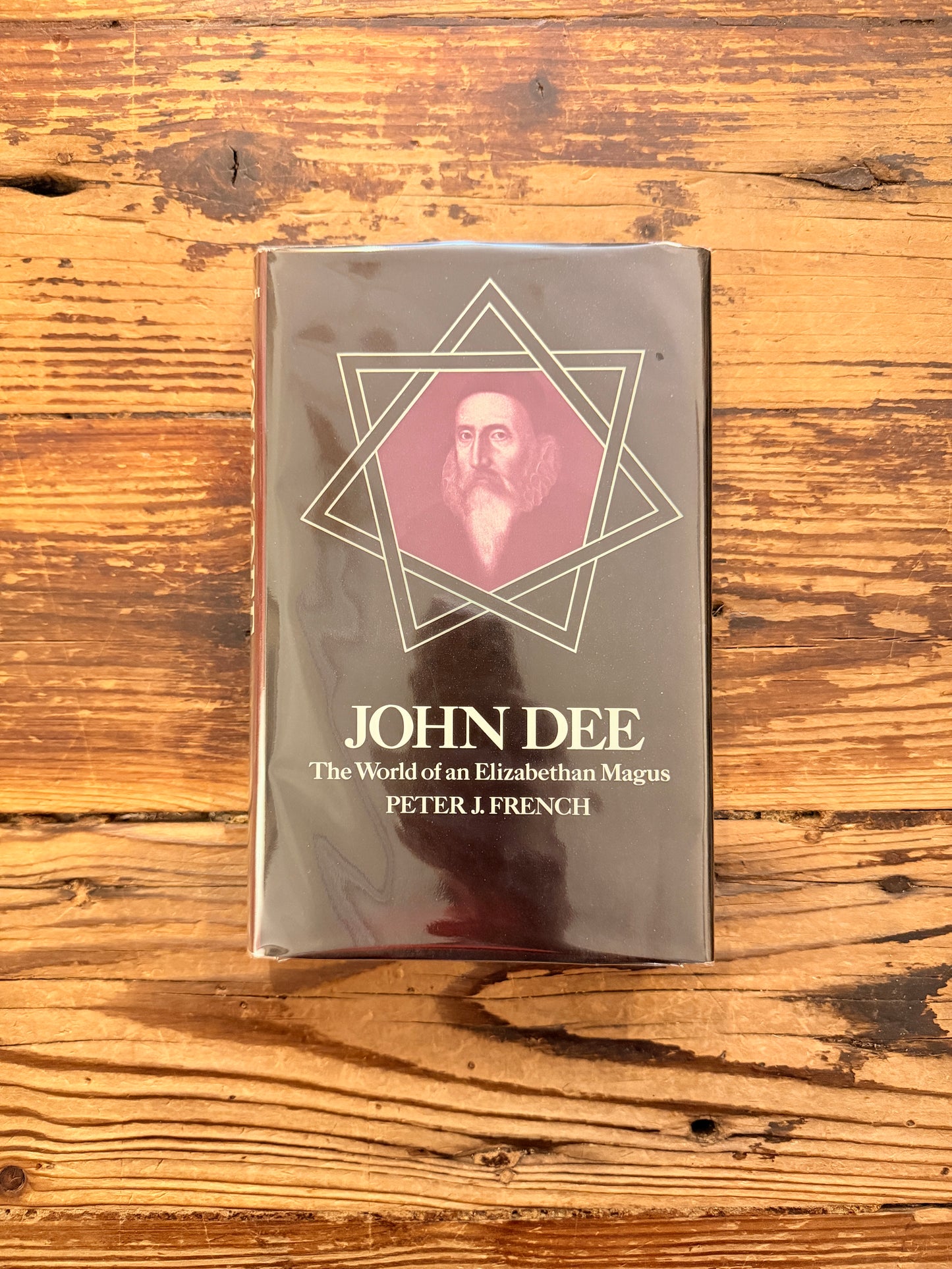 Front cover of a book titled 'John Dee: The World of an Elizabethan Magus' by Peter J. French on a wooden surface