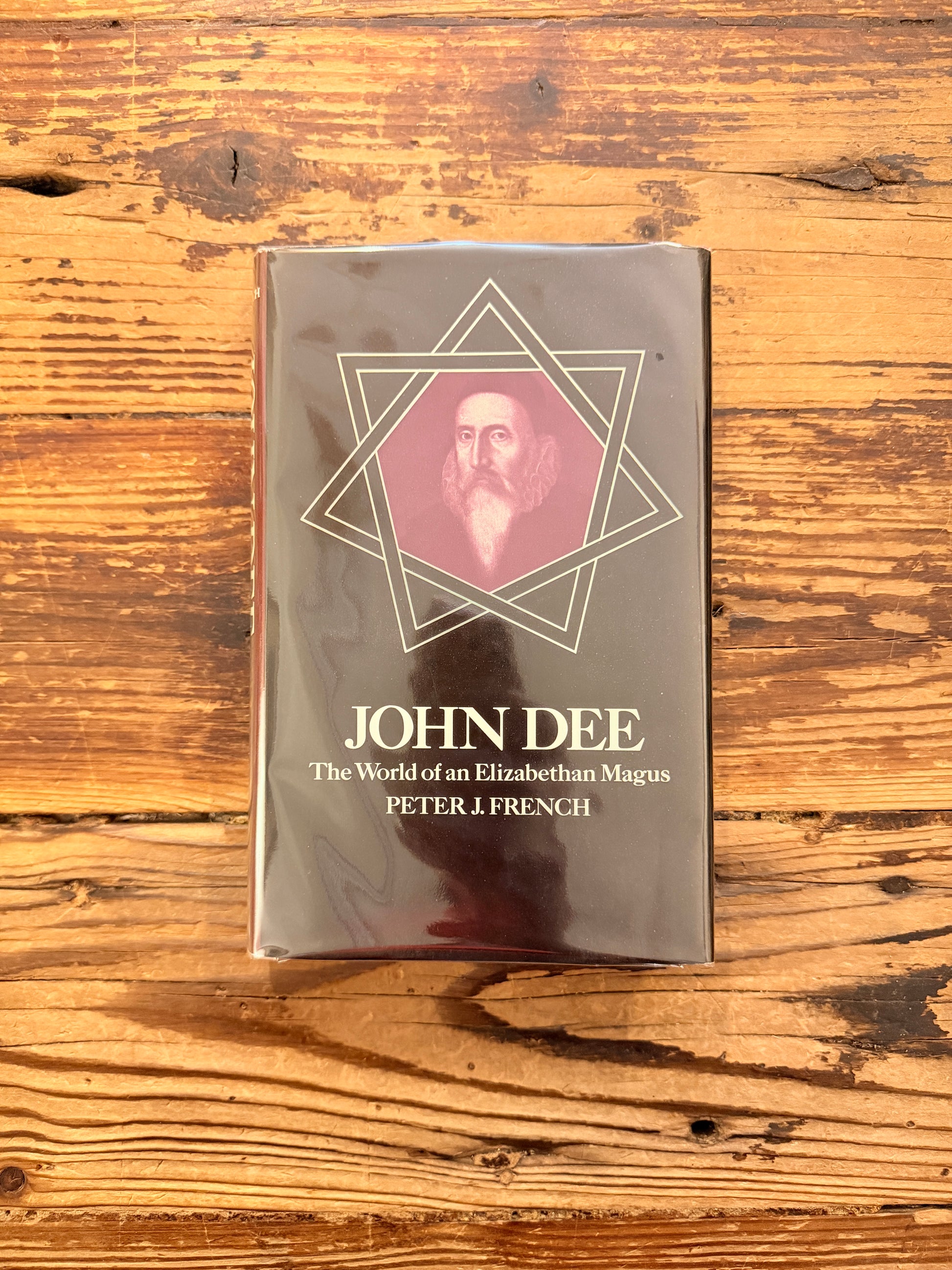 Front cover of a book titled 'John Dee: The World of an Elizabethan Magus' by Peter J. French on a wooden surface