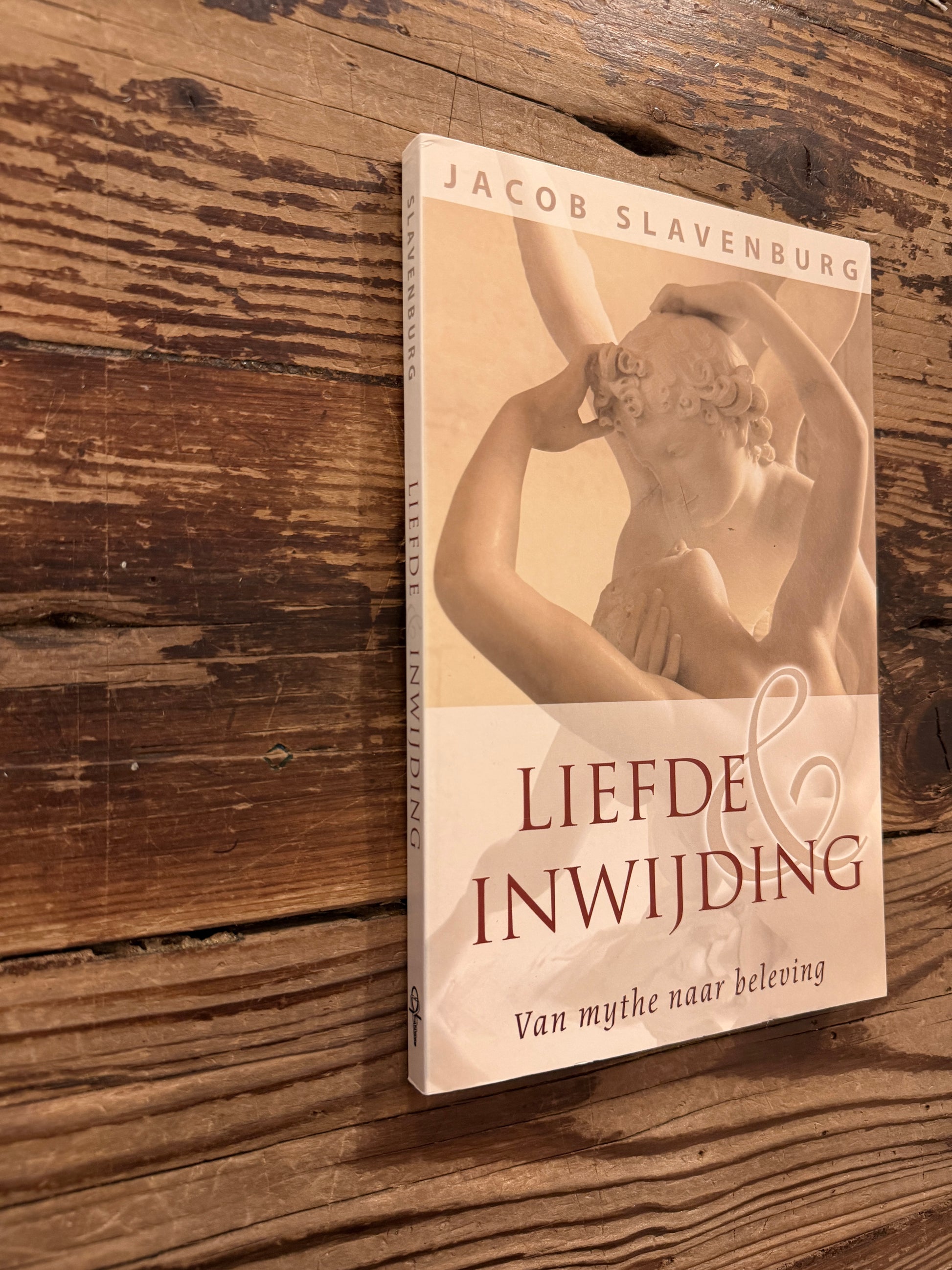 Voorkant en rug van boek met de titel 'liefde & inwijding, van mythe naar beleving' door Jacob Slavenburg op een houten achtergrond 