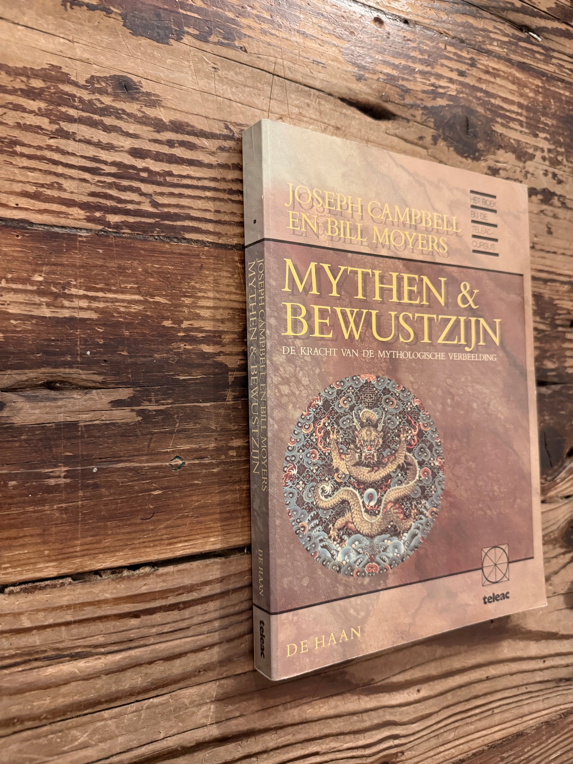 Voorkant en rug van boek met de titel 'mythen & bewustzijn' door Joseph Campbell en Bill Moyers op een houten achtergrond 