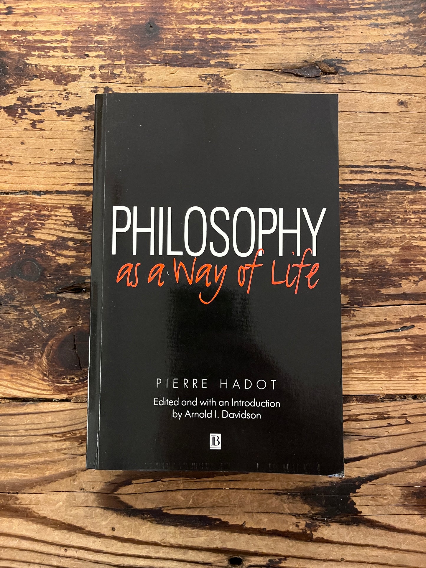 photo of the cover of the book "philosophy as a way of life" on a wooden background