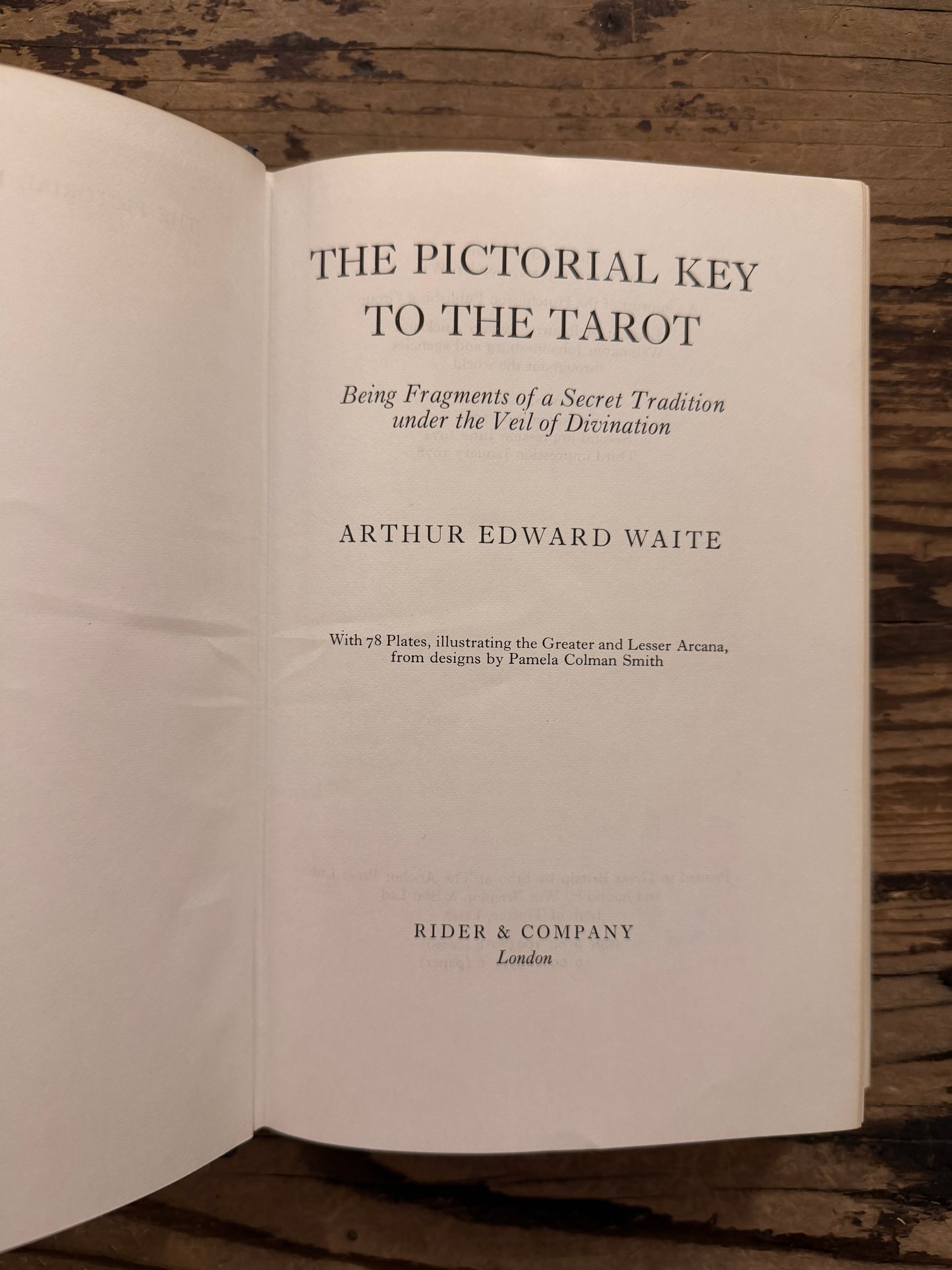 Open book titled 'The Pictorial Key to the Tarot' by A.E. Waite on a wooden surface 