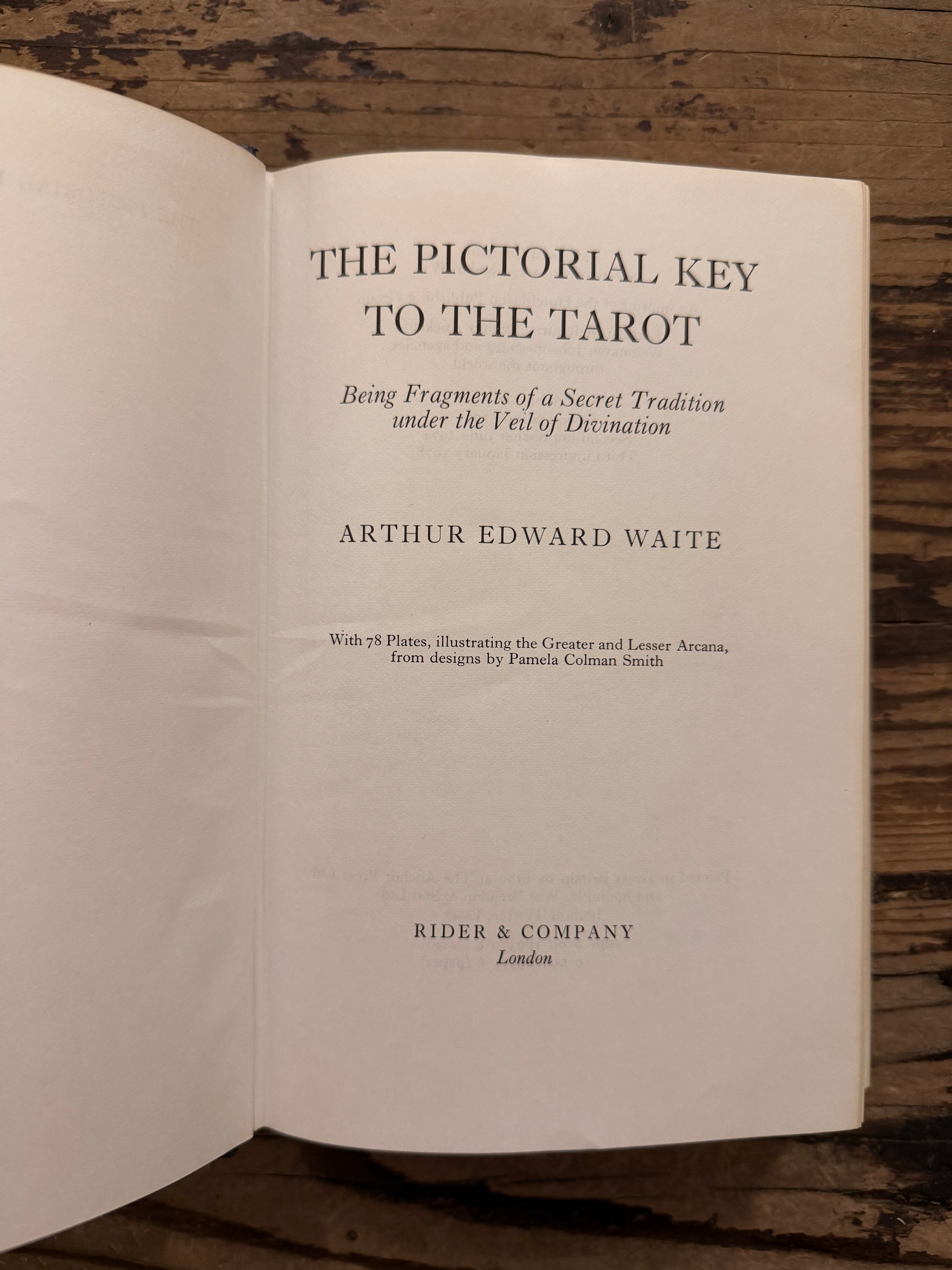 Open book titled 'The Pictorial Key to the Tarot' by A.E. Waite on a wooden surface 