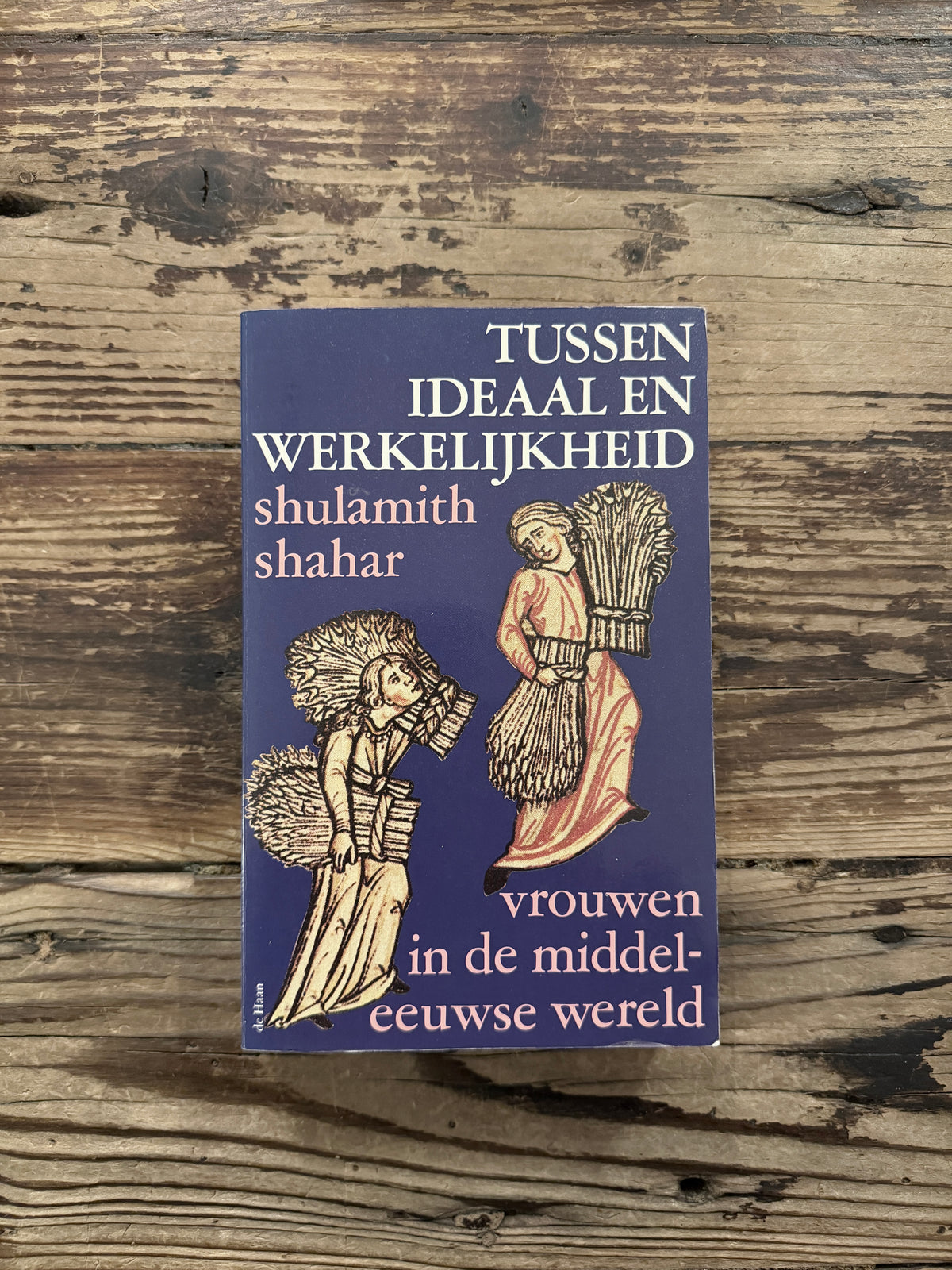 Voorkant van boek met de titel 'Tussen ideaal en werkelijkheid, vrouwen in de middeleeuwse wereld' door Shulamith Shahar op een houten achtegrond 