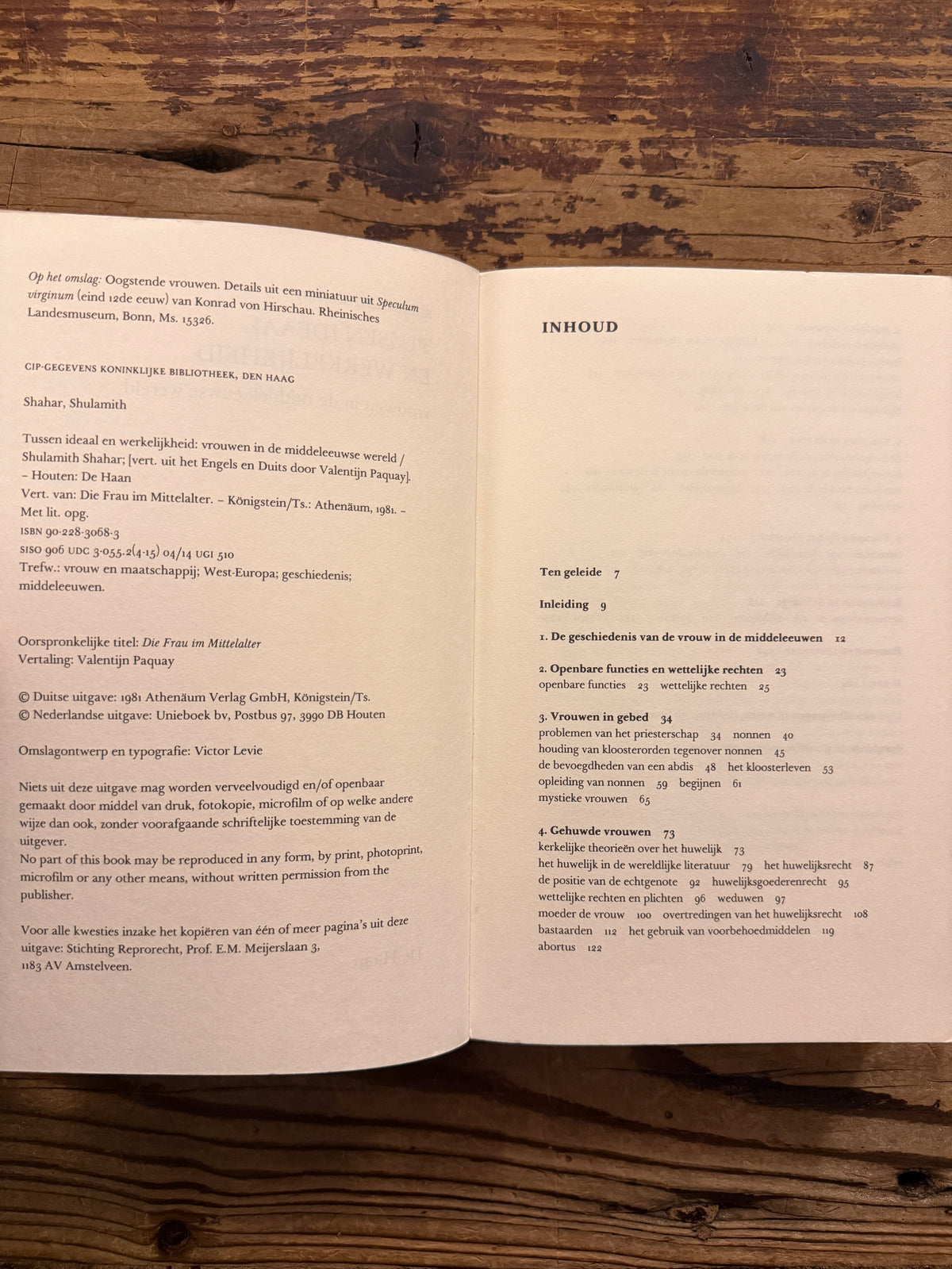 Open  boek met de titel 'Tussen ideaal en werkelijkheid, vrouwen in de middeleeuwse wereld' door Shulamith Shahar op een houten achtegrond 