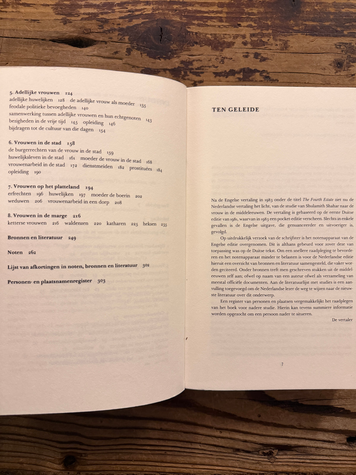 Open boek met de titel 'Tussen ideaal en werkelijkheid, vrouwen in de middeleeuwse wereld' door Shulamith Shahar op een houten achtegrond 